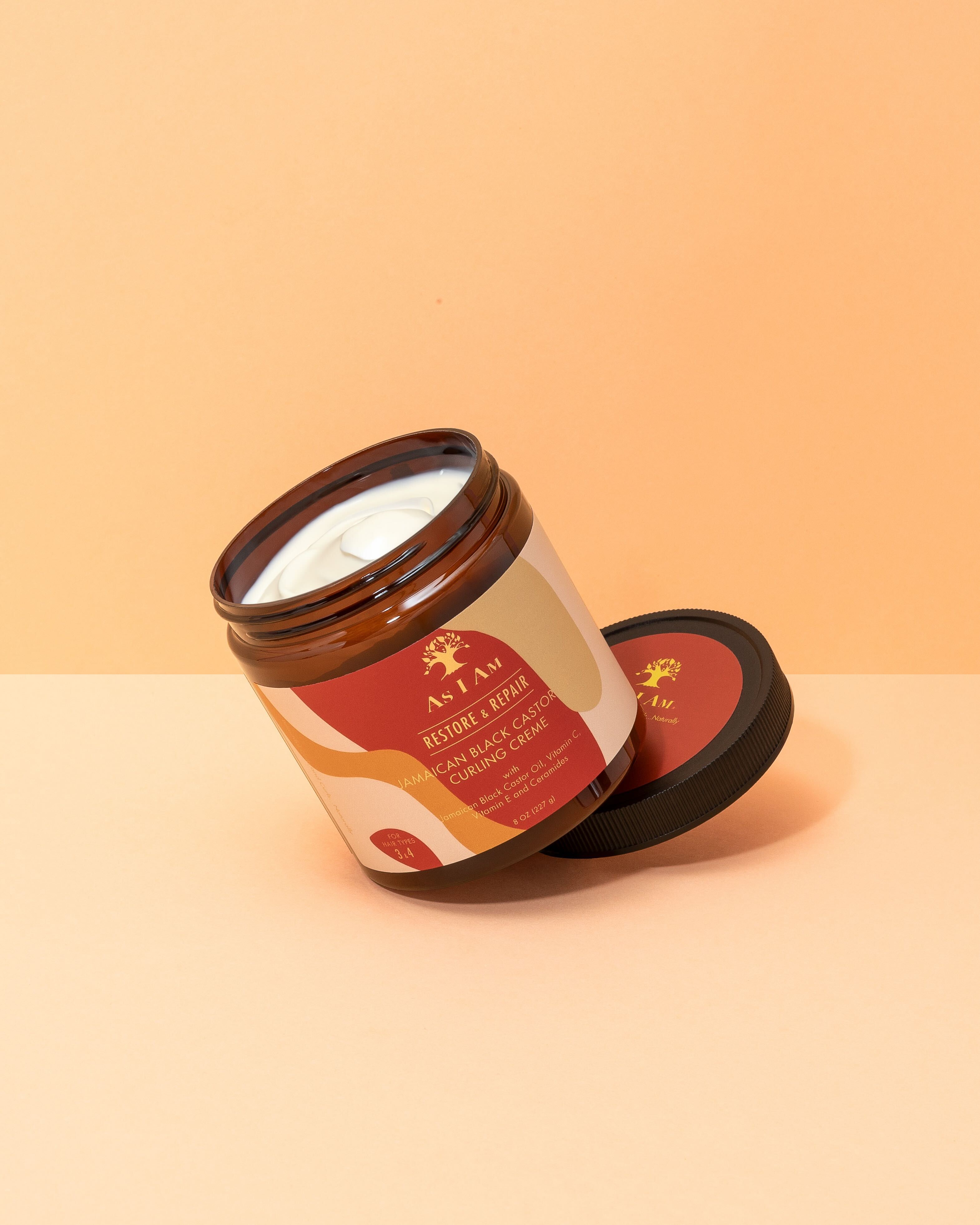 Åben dåse i plast fra As I Am Jamaican Black Castor Oil Curling Creme. Hvid creme i brun dåse med rød etiket og sort låg.