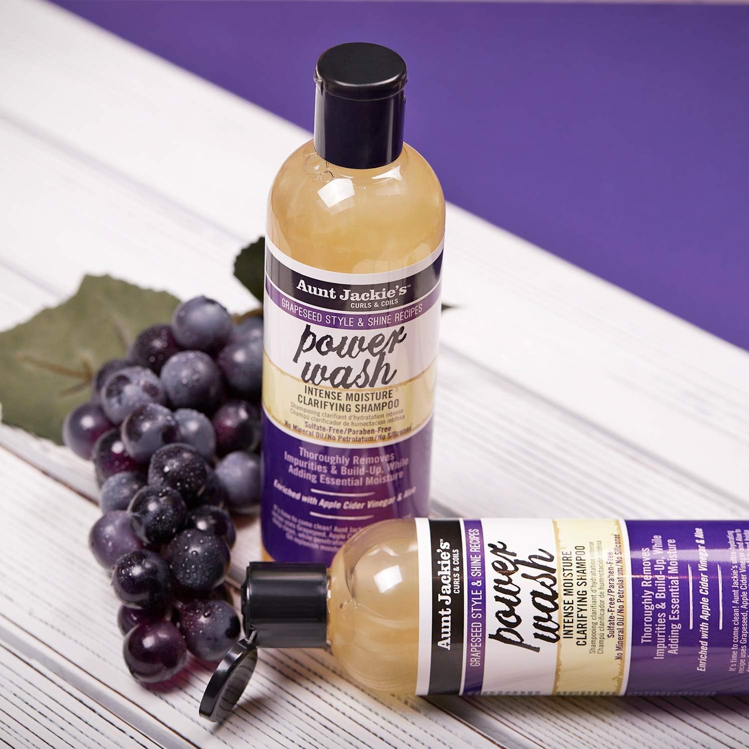To flasker Aunt Jackie's Power Wash Intense Moisture Clarifying Shampoo, stående og liggende, med en klynge mørke druer ved siden af.