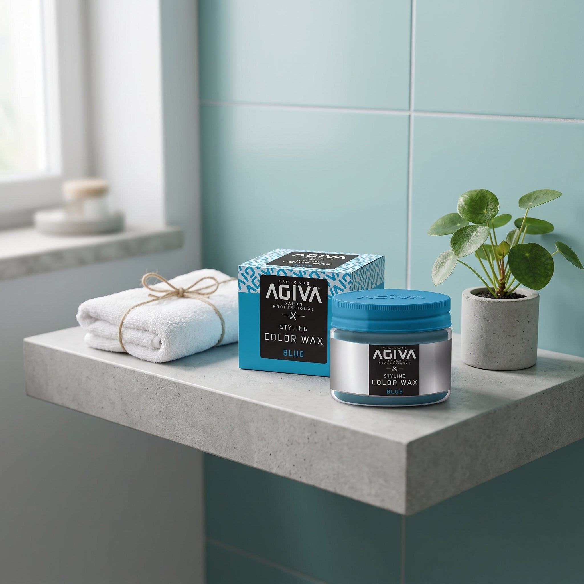 AGIVA Styling Color Wax Blue i glas med blåt låg ved siden af emballage, hvidt håndklæde og grøn plante på badeværelsesbord.