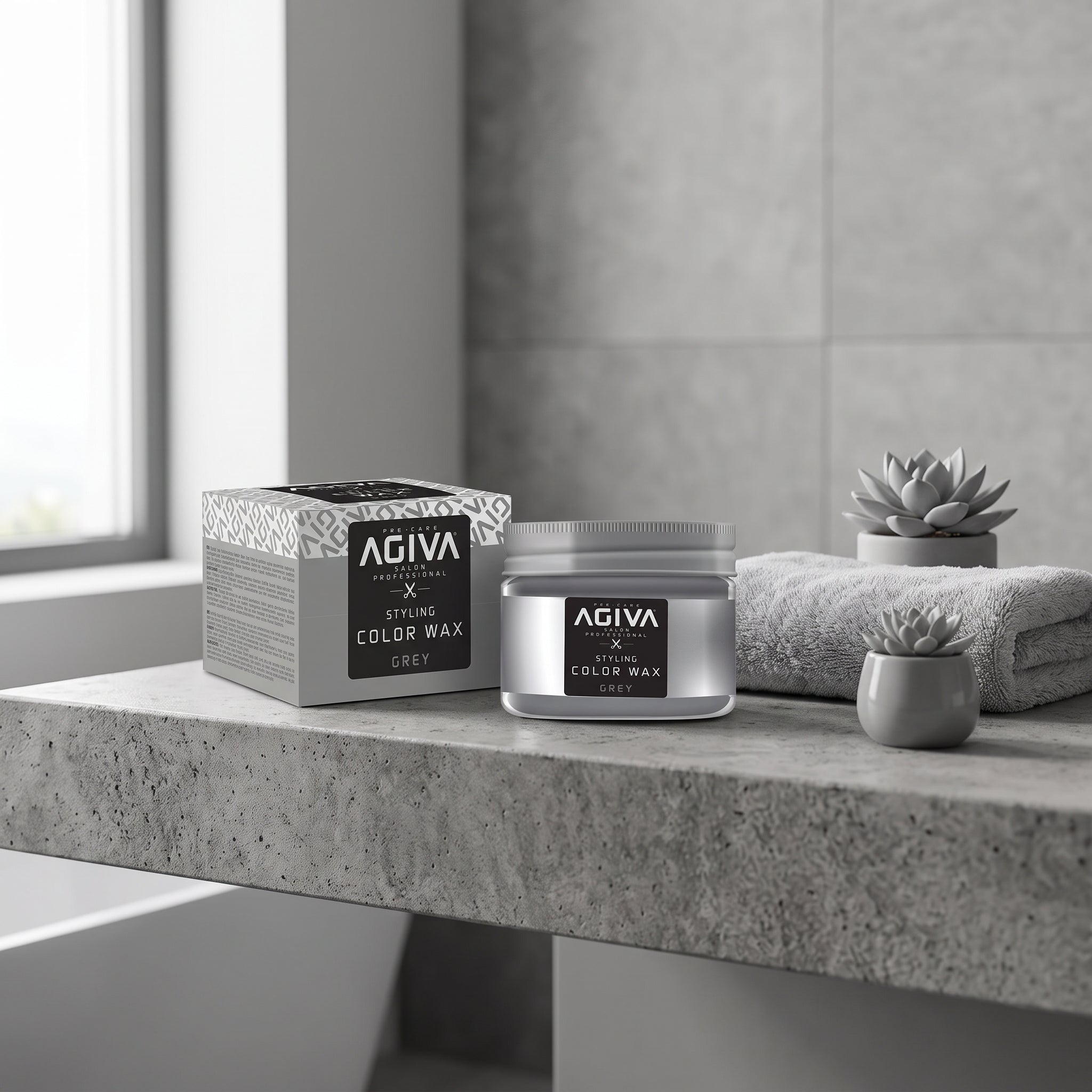 AGIVA Styling Color Wax Grey i sølvglas ved siden af æske på betonbord med håndklæde og succulenter.
