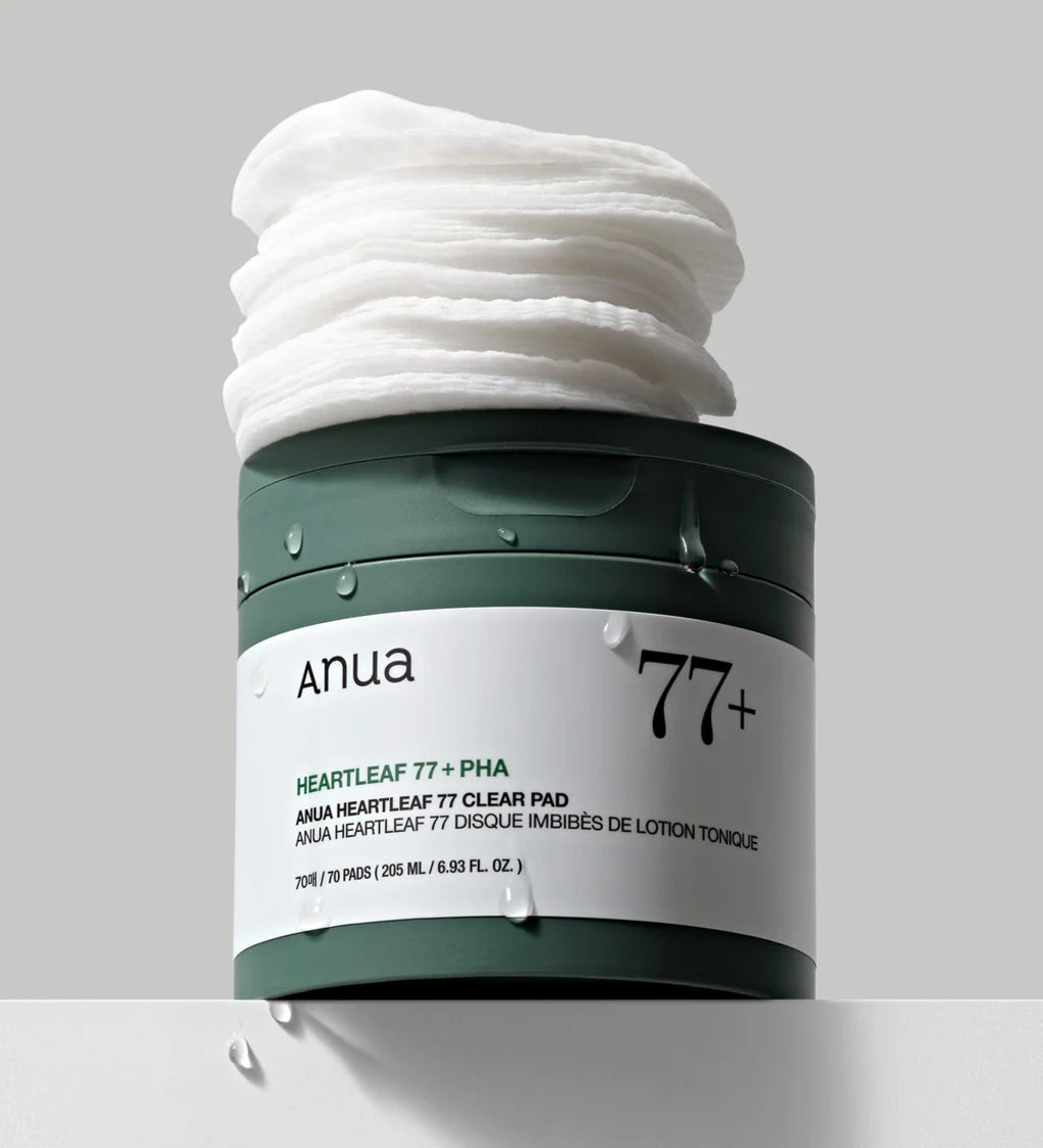 Anua Heartleaf 77 Clear Pad i grøn beholder med låg åbent og stakke af toner-gennemvædede rondeller ovenpå.