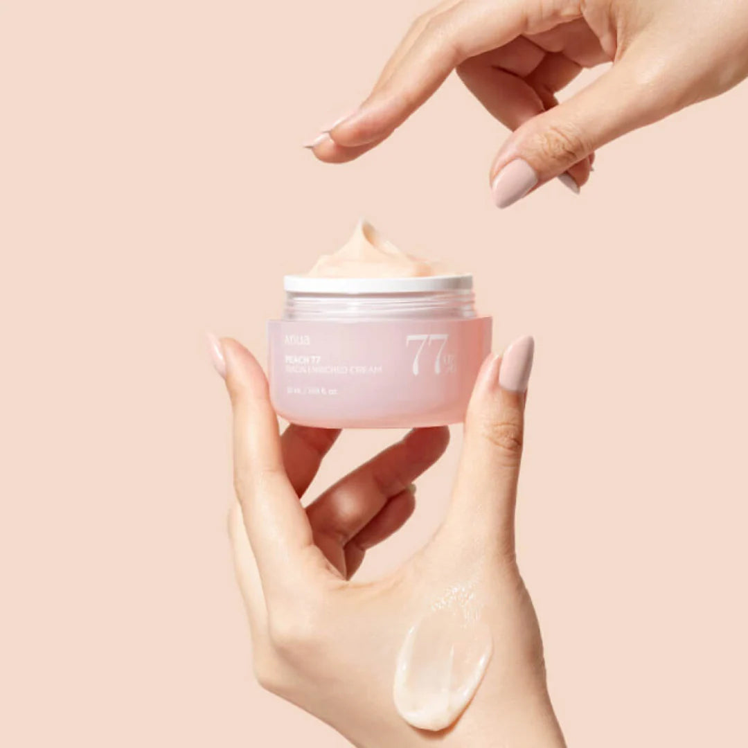 Hand applies Anua Peach 77 Niacin Enriched Cream 50ml from pink jar with creamy peach consistency.