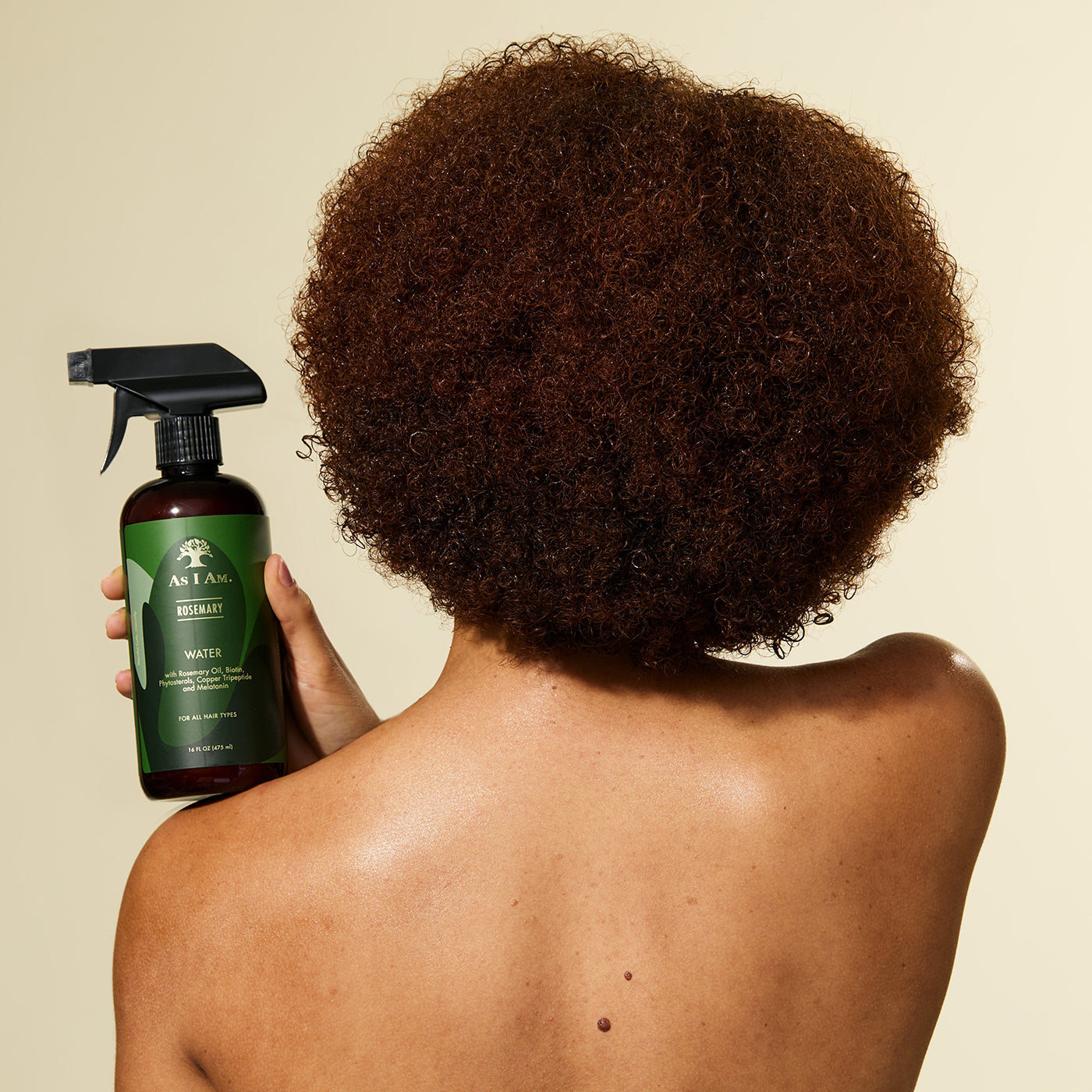 En person med krøllet hår holder en flaske As I Am Rosemary Water Spray (475 ml) og er ved at spraye produktet i håret.