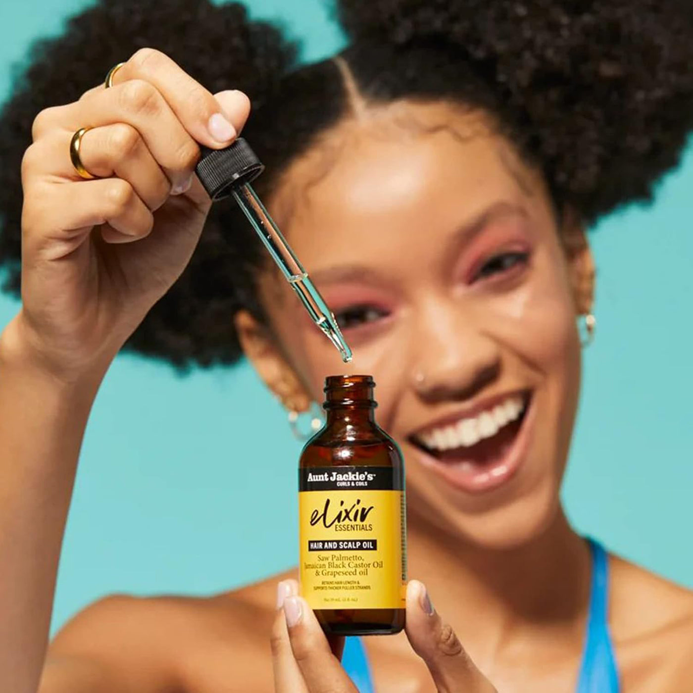 Nærbillede af en hånd, der drypper Aunt Jackie's Elixir Essentials Hair and Scalp Oil fra en pipette ned i en brun glasflaske.
