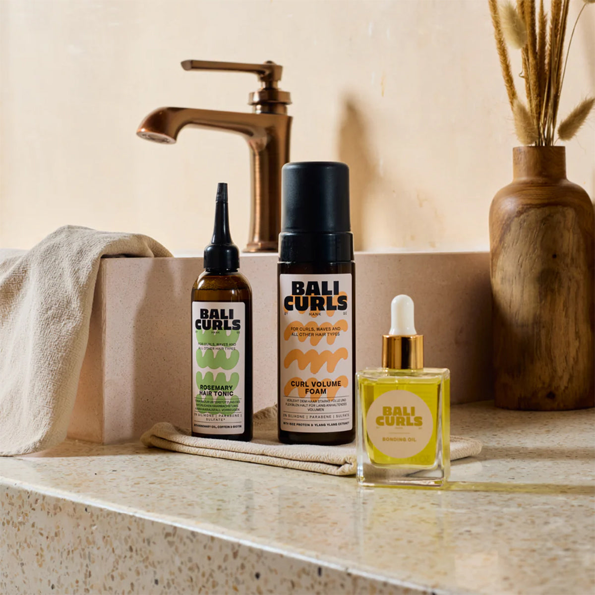 BALI CURLS products on bathroom table – Rosemary Hair Tonic, Curl Volume Foam** and Bonding O in natural light.
