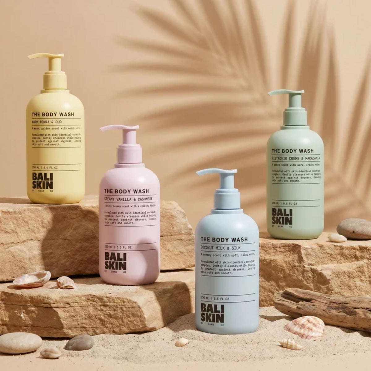 Fire Bali Skin body wash-flasker i gul, lyserød, blå og grøn på sten og sand med skaller.