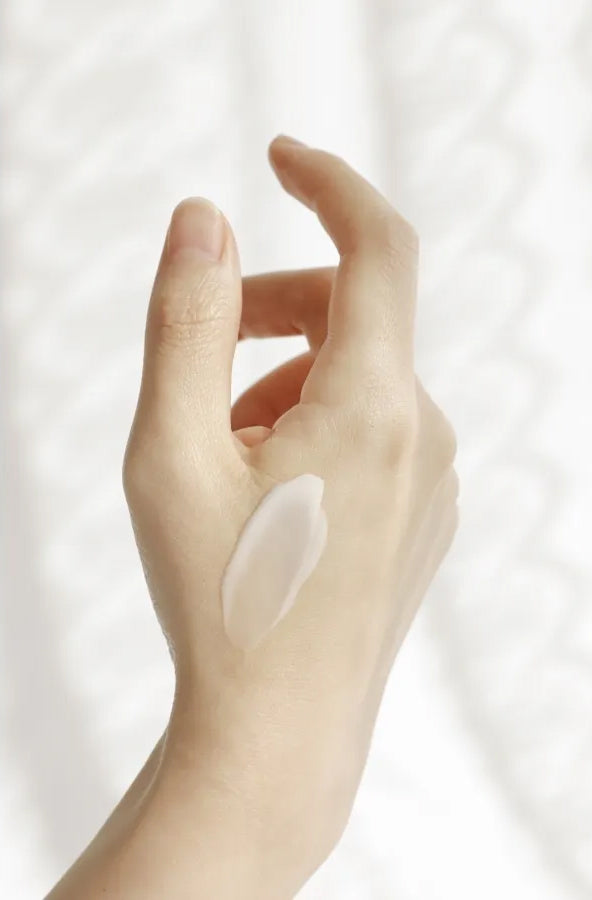 Hånd med påført Beauty of Joseon Dynasty Cream 50ml viser cremet konsistens i blød belysning mod hvid baggrund.