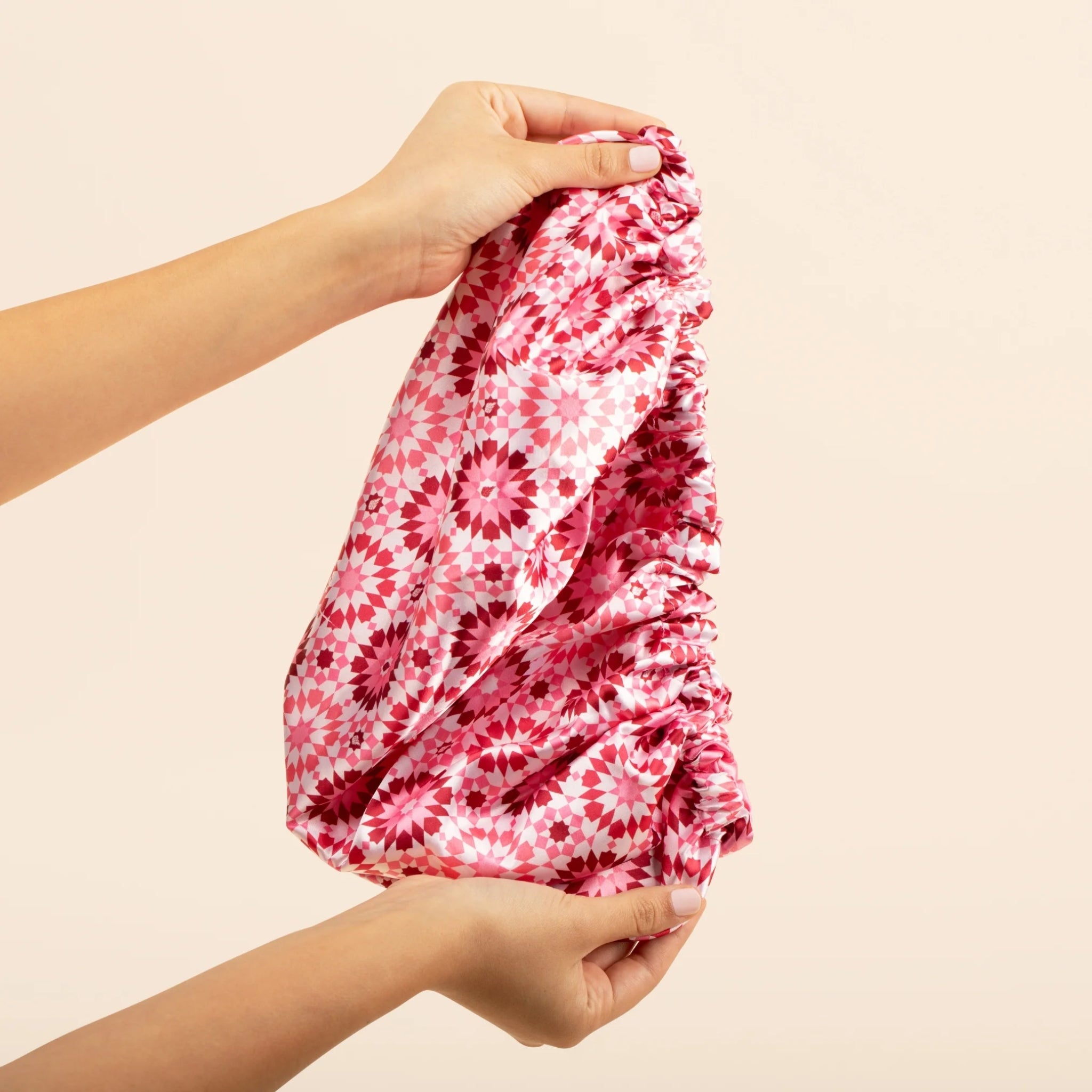 Kvinde holder sammenpakket pink blomstret opbevaringstaske med daisy-mønster mod beige baggrund.