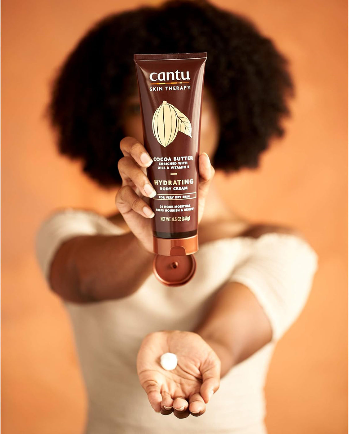 Kvinde holder Cantu Skin Therapy Cocoa Butter Hydrating Body Cream.