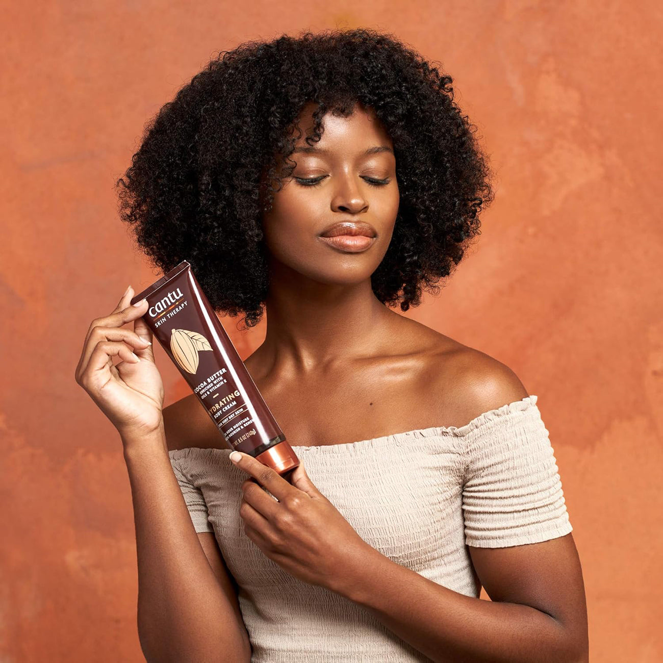 Kvinde der holder en flaske Cantu Skin Therapy Cocoa Butter Body Cream.