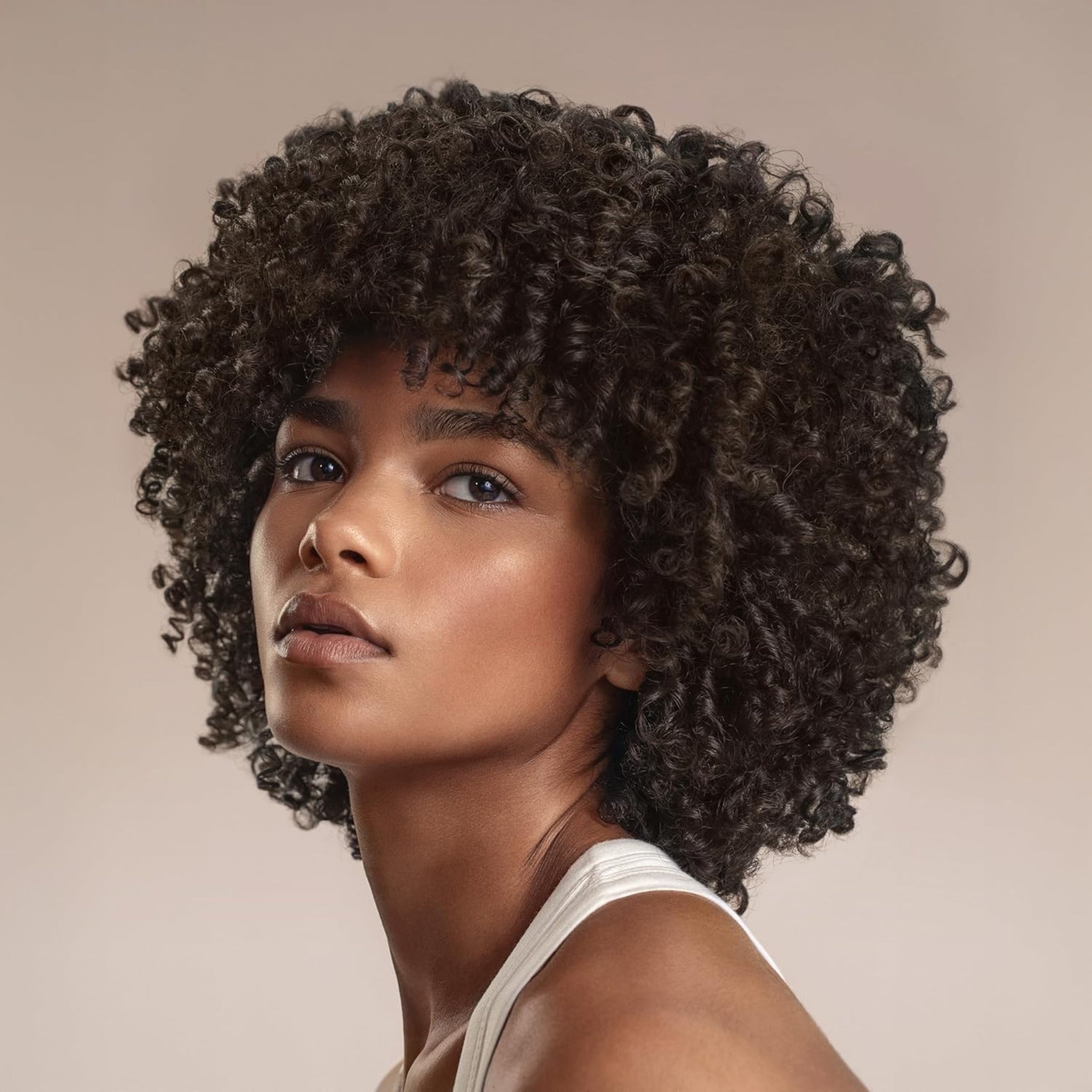 Kvinde med naturligt krøllet afro-hår i mørkebrun nuance og curtain bangs, iført hvid top.