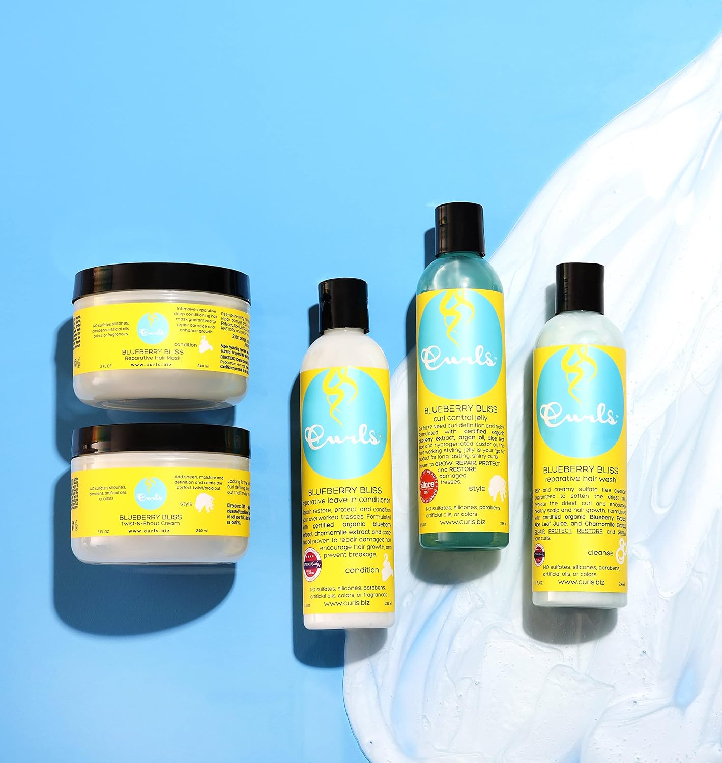 Fire Curls Blueberry Bliss-produkter: To krukker med jelly/paste, en flaske olie og en flaske leave-in conditioner på lyseblå baggrund.
