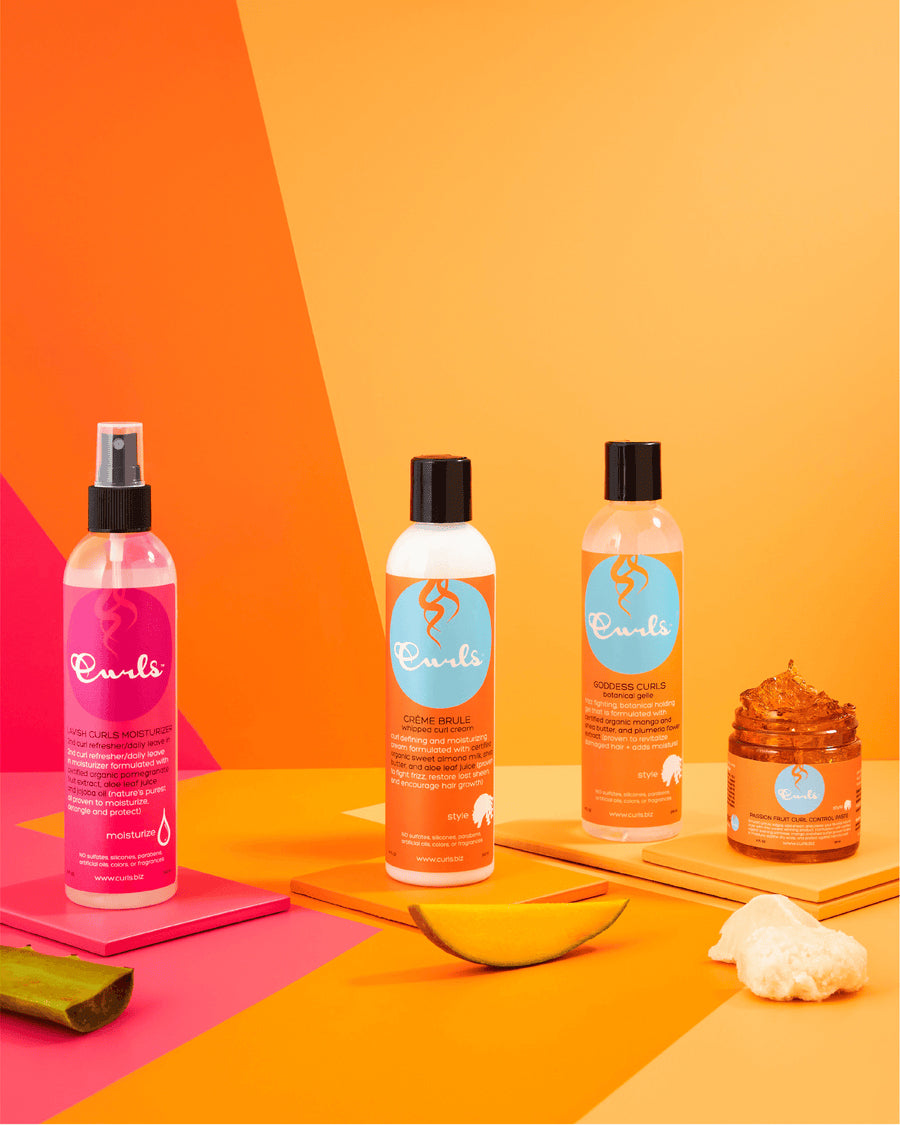 Curls hårplejeprodukter: Lavish Curls Moisturizer (pink spray), Curl Milk og Curl Gel flasker samt en beholder med styling produkt. Farverig baggrund.