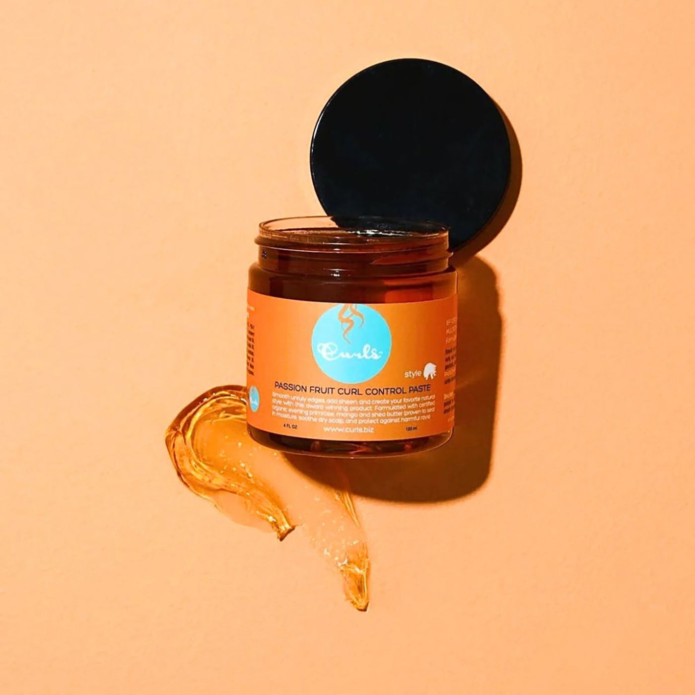 Curls Passion Fruit Curl Control Paste (120 ml) i åben krukke på orange baggrund med passionsfrugt. Styling paste til definerede krøller.