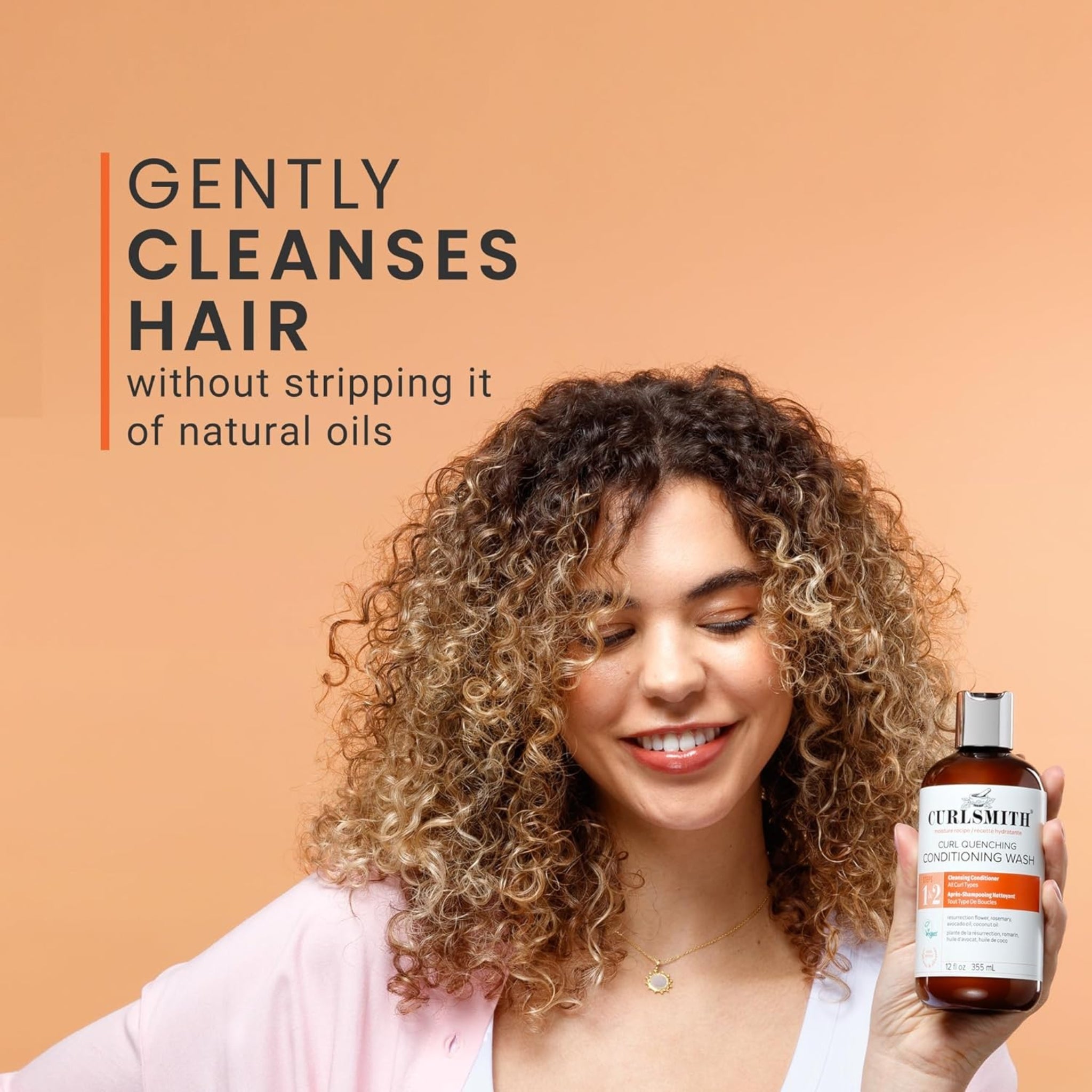 Kvinde med krøllet hår smiler og holder Curlsmith Curl Quenching Conditioning Wash, der rengør håret skånsomt uden at fjerne naturlige olier.