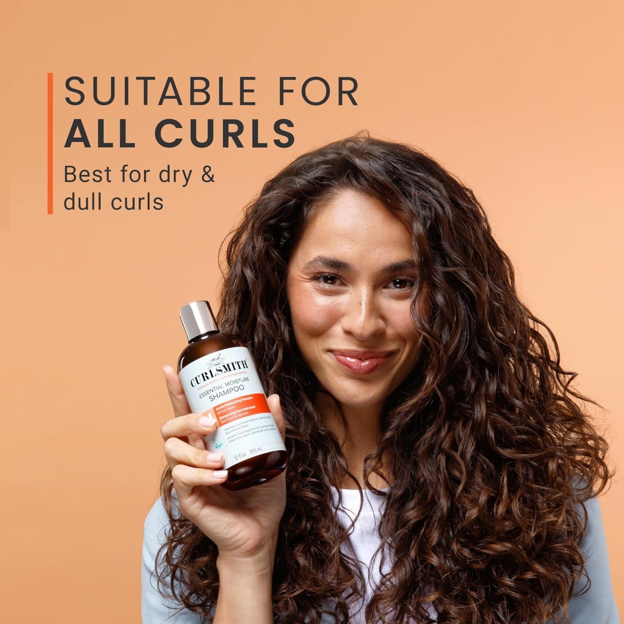 Kvinde med krøllet hår holder Curlsmith Essential Moisture Shampoo, velegnet til alle krøller, bedst til tørt og mat hår.