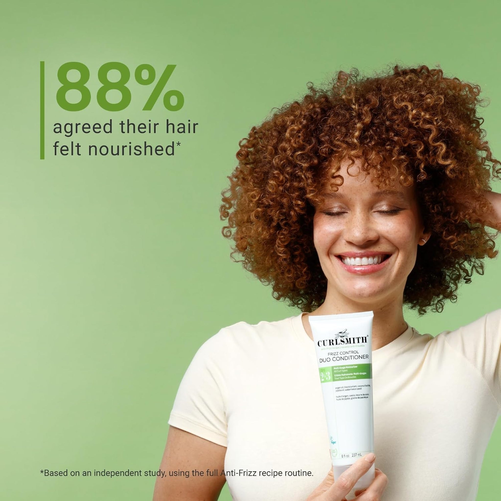 Kvinde med krøllet rødbrunt hår smiler og holder Curlsmith Frizz Control Duo Conditioner, 88% oplevede nourished hair.