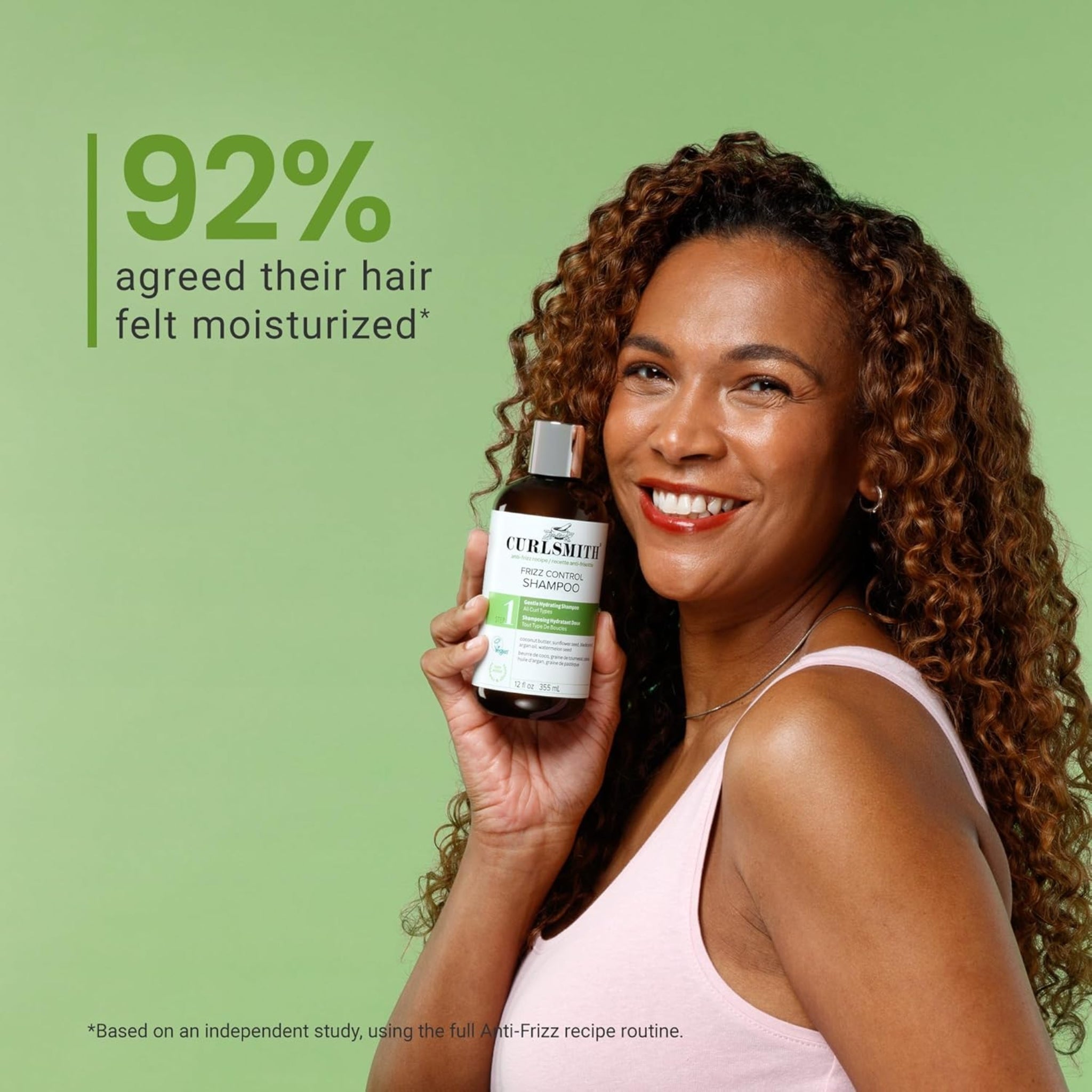 Kvinde med krøllet hår smiler og holder Curlsmith Frizz Control Shampoo, 92% oplevede mere fugtigt hår.