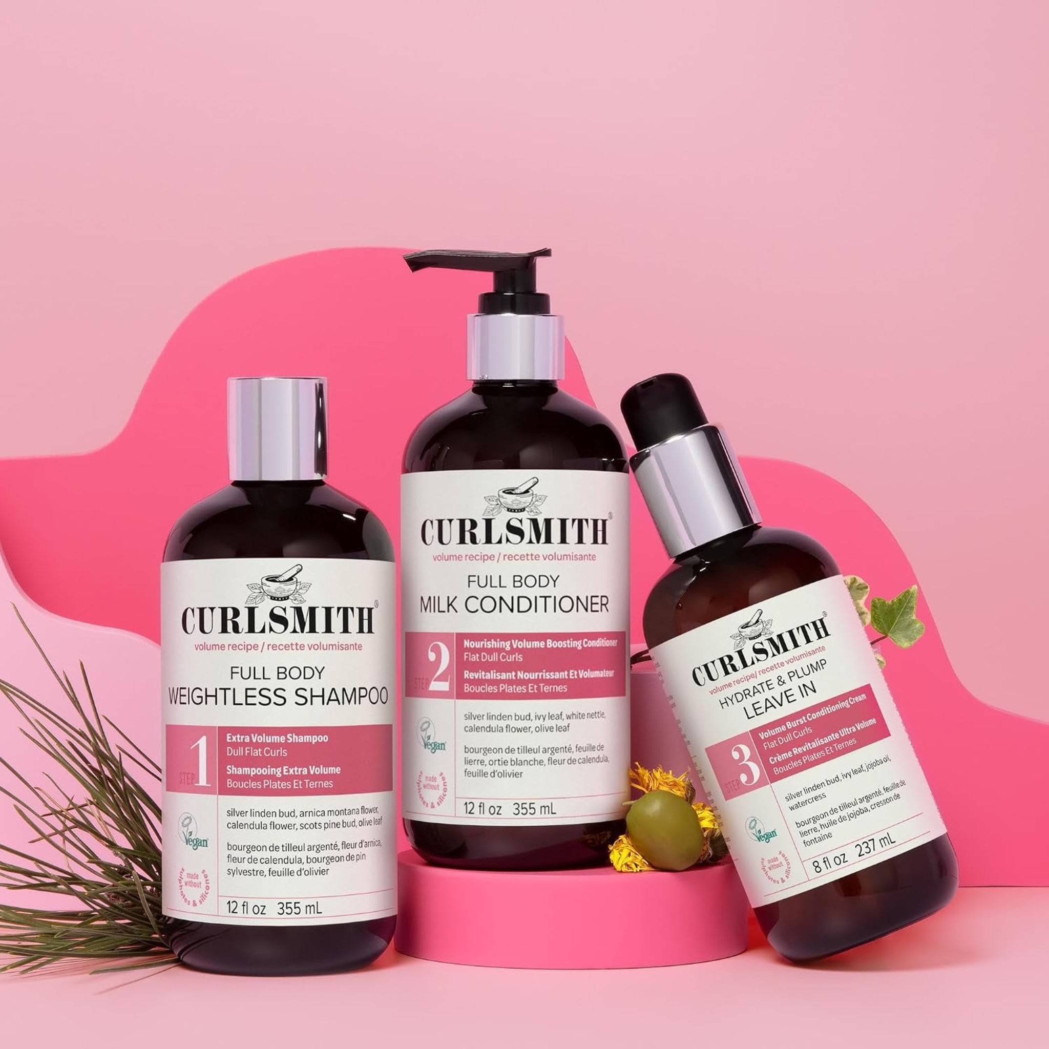 Curlsmith Full Body volumen hårplejeserie: shampoo, mælkebalsam og leave-in creme i mørke flasker på lyserød baggrund.