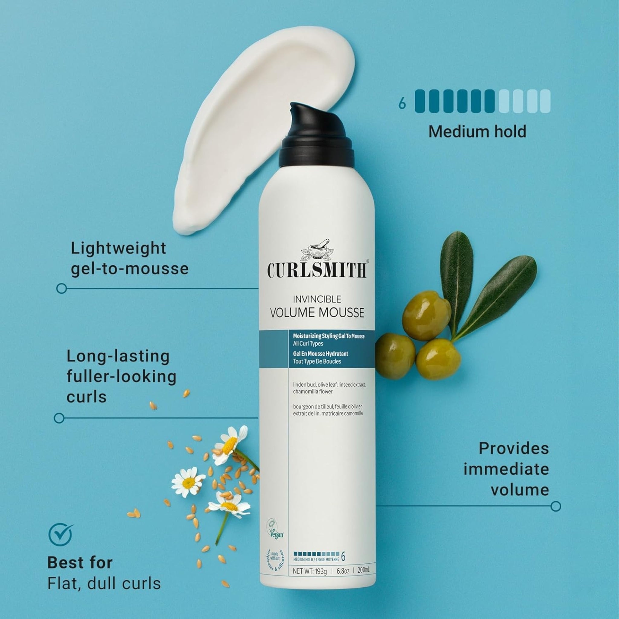 Curlsmith Invincible Volume Mousse i hvid flaske med sort pumpe, omgivet af oliven, kamille og hørfrø på lyseblå baggrund.