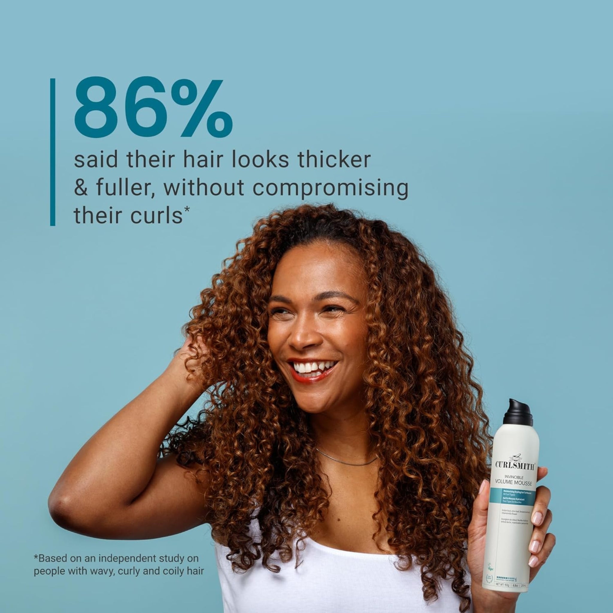 Kvinde med krøllet hår smiler og holder Curlsmith Invincible Volume Mousse – 86% oplevede tykkere, fyldigere krøller.