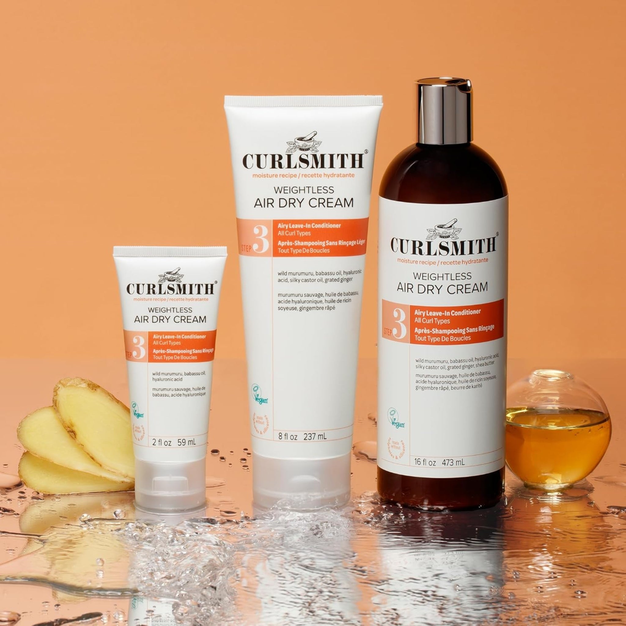 Curlsmith Weightless Air Dry Cream i tre størrelser med ingefær og olie på vandreflekterende overflade, orange baggrund.