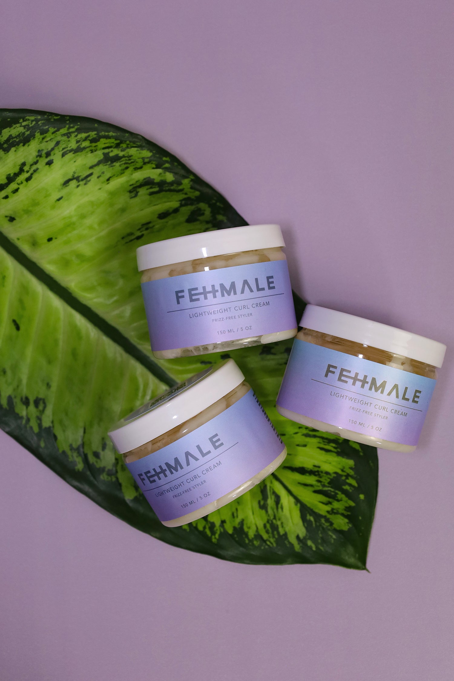 Tre Fehmale Lightweight Curl Cream 150ml krukker på grøn bladdekoration mod lilla baggrund, perfekt til krøllet hår.