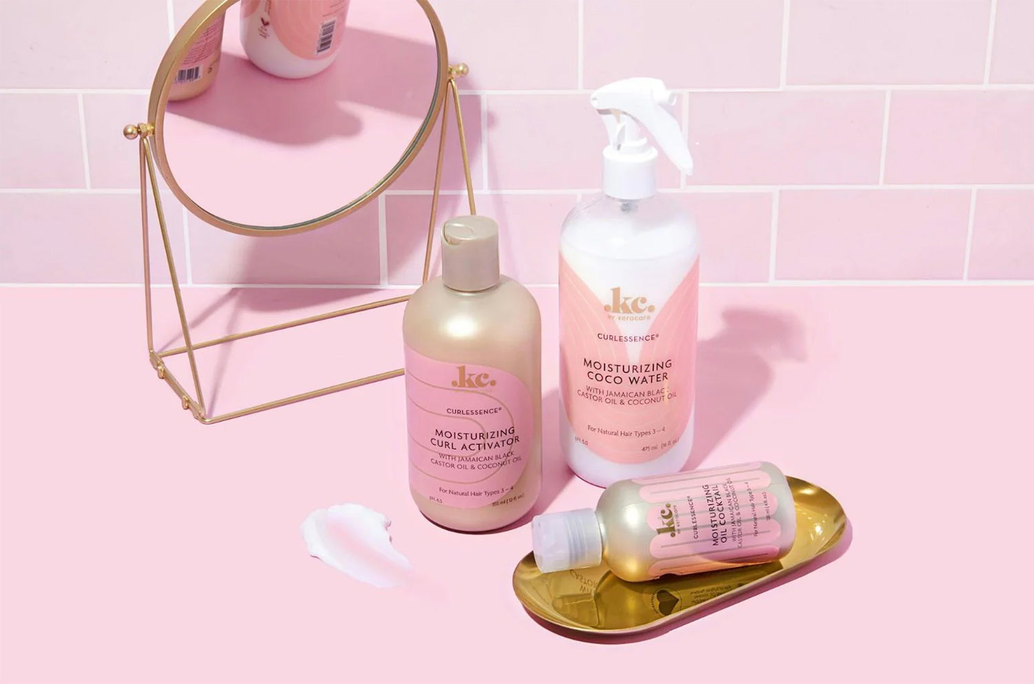 Keracare Curlessence Moisturizing Curl Activator, Coco Water og Oil Cocktail præsenteret på en lyserød baggrund med et spejl.