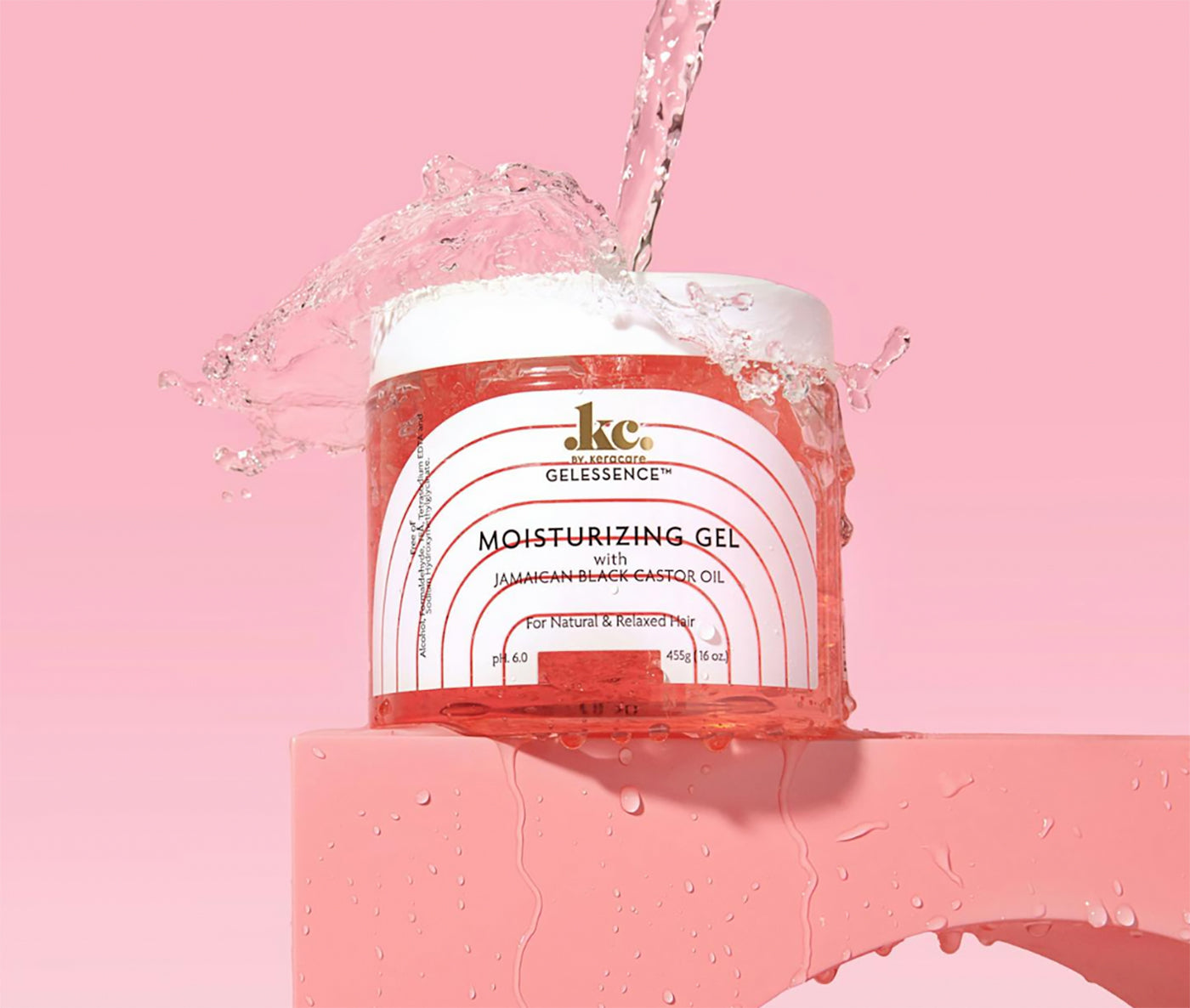 Klar beholder med KeraCare Gelessence Moisturizing Gel. Vand sprøjter op omkring beholderen på en lyserød baggrund, der fremhæver produktets fugtgivende egenskaber.
