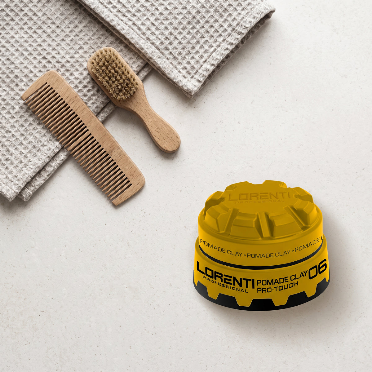 Lorenti Professional Pomade Clay Pro-Touch 06 i gul krukke ved siden af træbørste, kam og beige håndklæder.