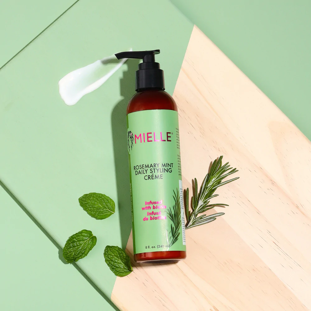 Mielle Rosemary Mint Multi-Vitamin Daily Styling Crème (240 ml) vises med en klat creme, der demonstrerer produktets konsistens. Fremhæver naturlige ingredienser som mynte og rosmarin.