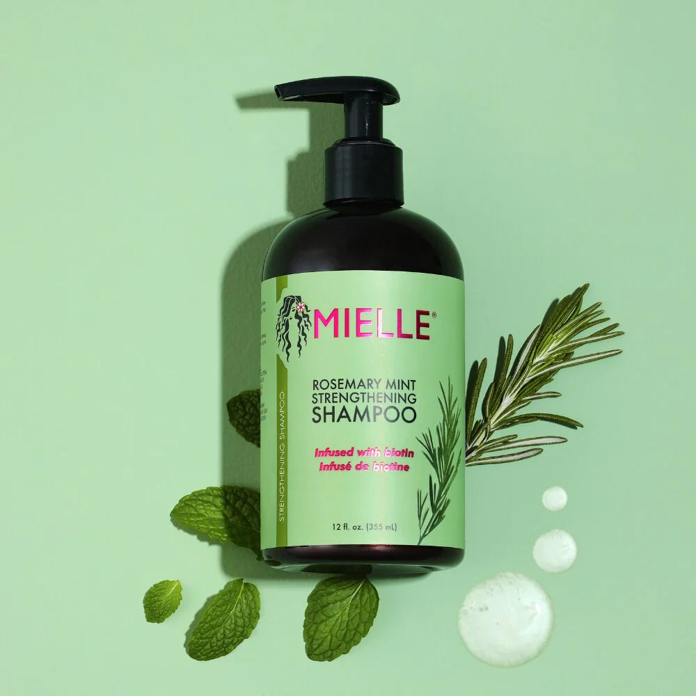 Flaske Mielle Rosemary Mint Strengthening Shampoo (355 ml) med sort pumpe, grøn etiket, rosmarin, mynteblade og lysegrøn baggrund.
