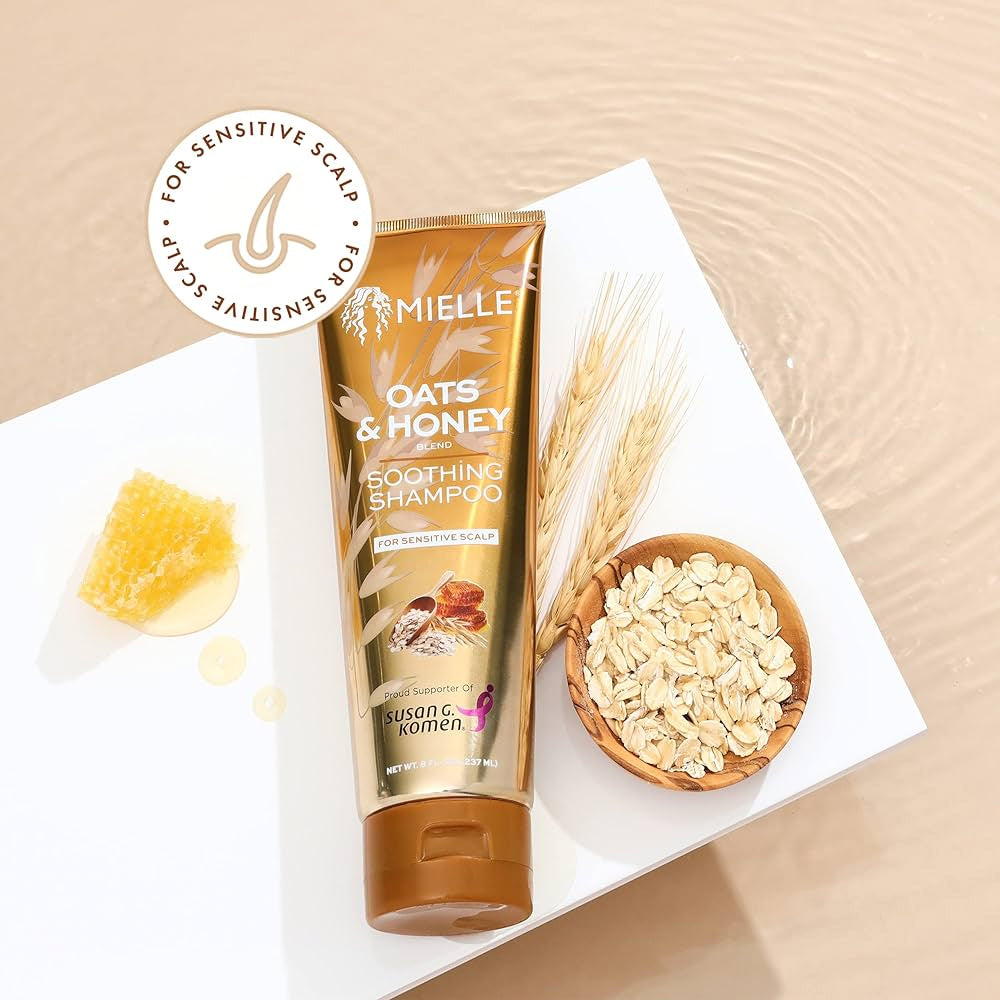 Mielle Oats & Honey Soothing Shampoo 237ml placeret på hvid overflade med havre, honning og hvedestrå ved siden af.