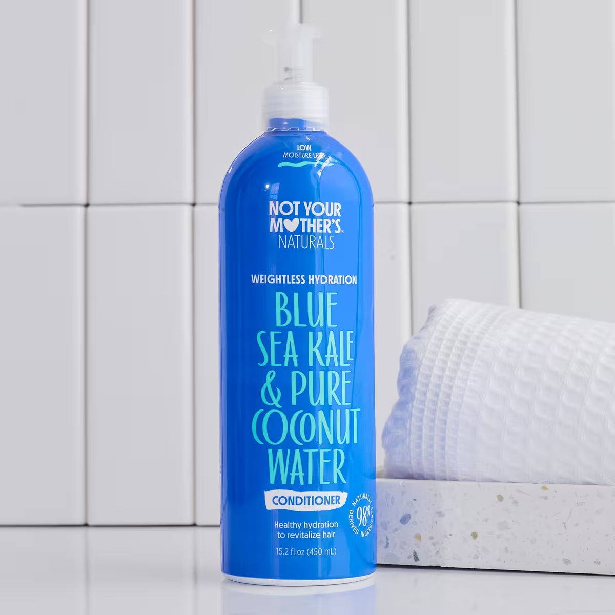 En blå flaske Not Your Mother's Naturals Blue Sea Kale & Pure Coconut Water Weightless Hydration Conditioner foran en hvid baggrund med fliser.