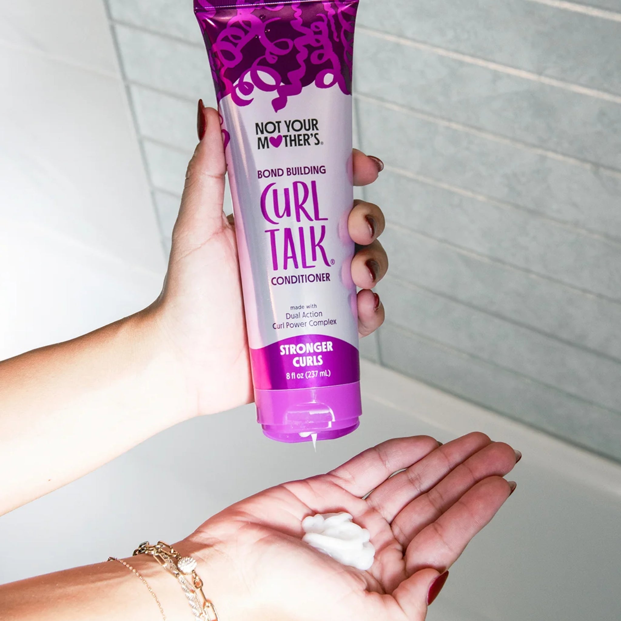 Not Your Mother's Curl Talk Bond Building Conditioner klemmes ud i hånd med lilla tube i baggrund.