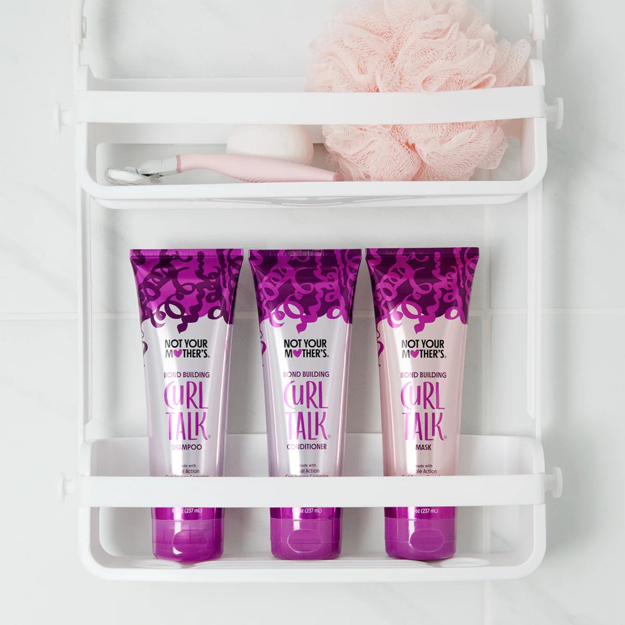 Not Your Mother's Curl Talk shampoo, conditioner og mask i lilla tuber på hvid badehylde med pink svamp.