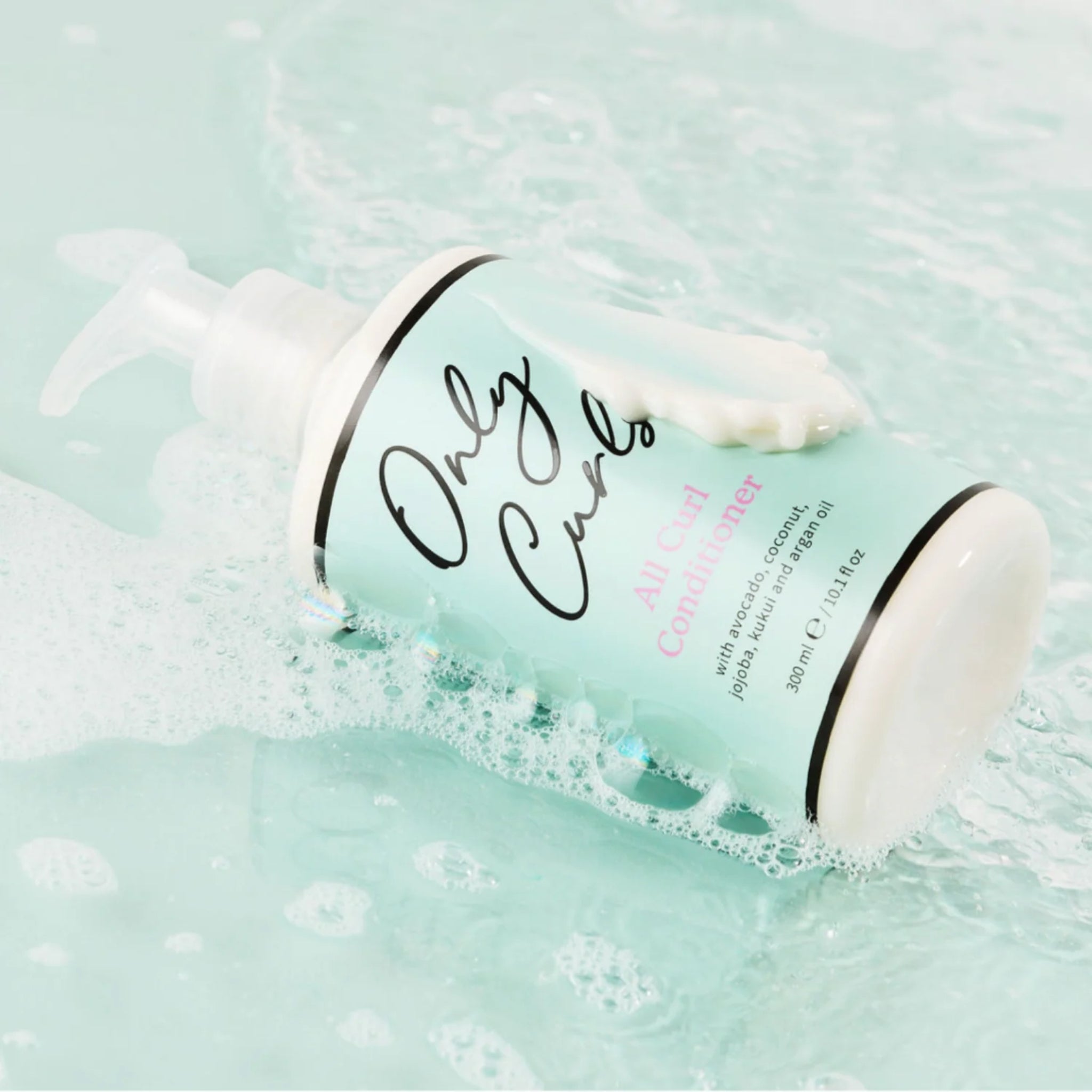 Only Curls All Curl Conditioner-flaske ligger i skummende vand med cremet hårbalsam der siver ud af pumpen.