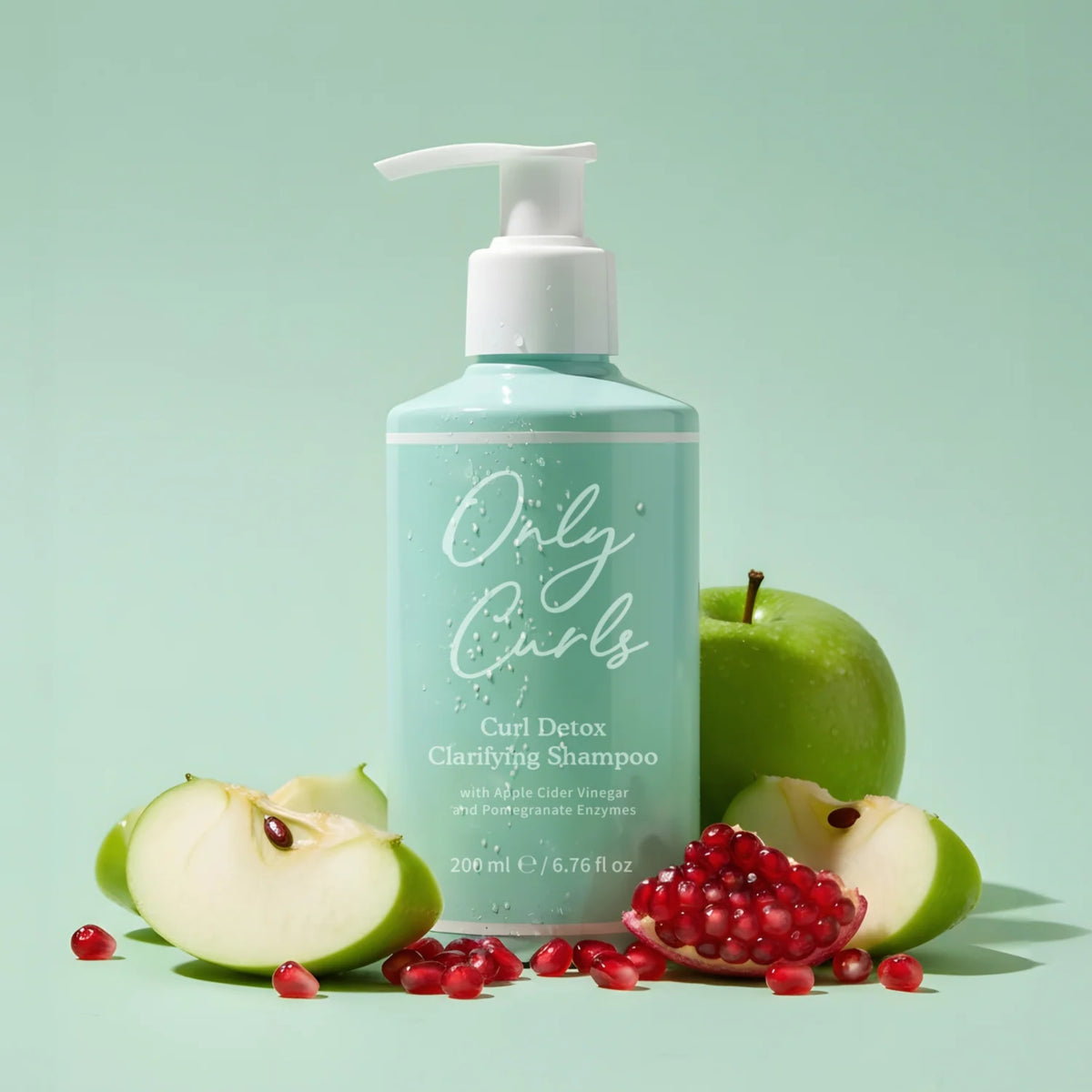 Only Curls Curl Detox Clarifying Shampoo flaske omgivet af grønne æbler og granatæblekerner på mintgrøn baggrund.