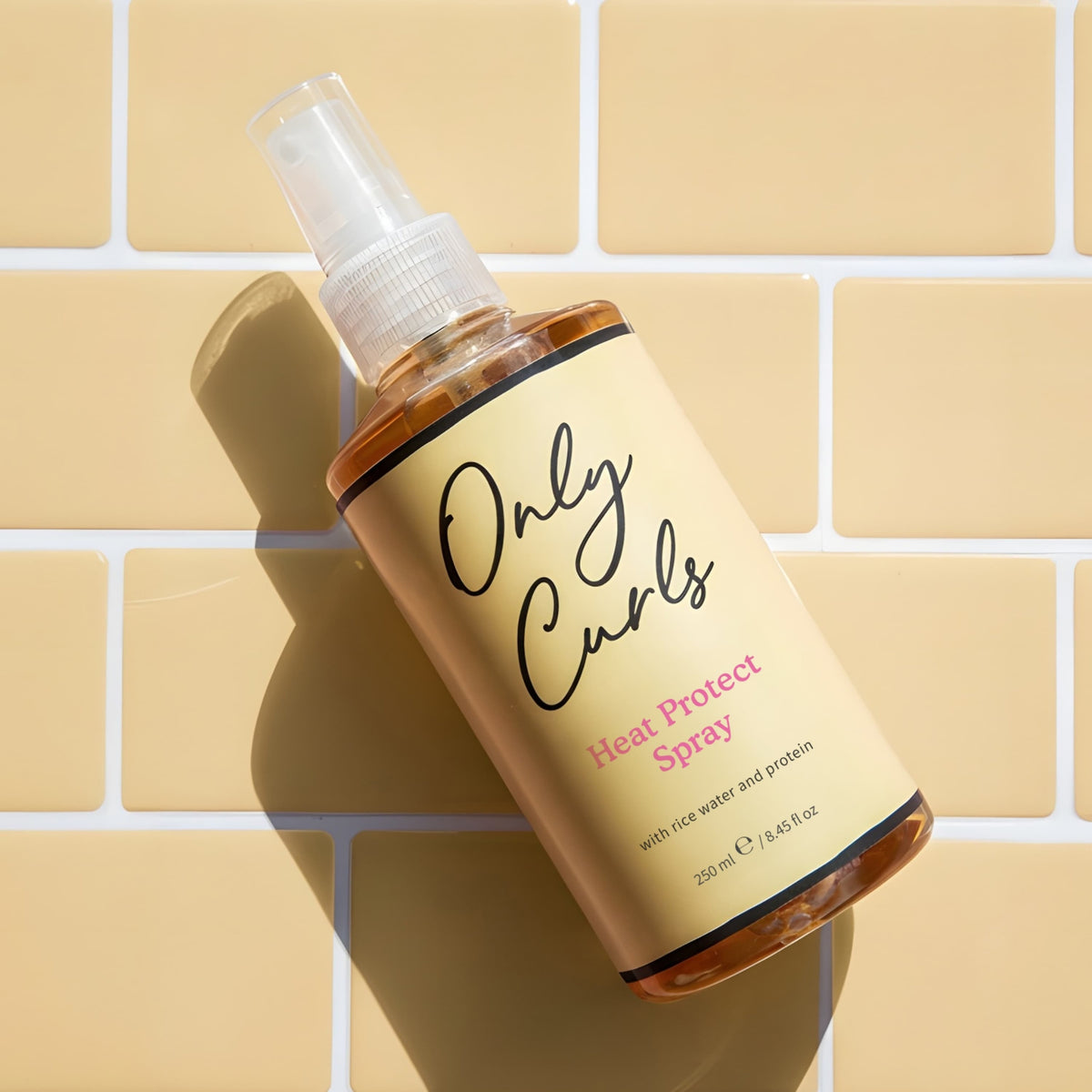 Only Curls Heat Protect Spray, 250 ml sprayflaske med rismælk og protein, ligger på gule fliser.