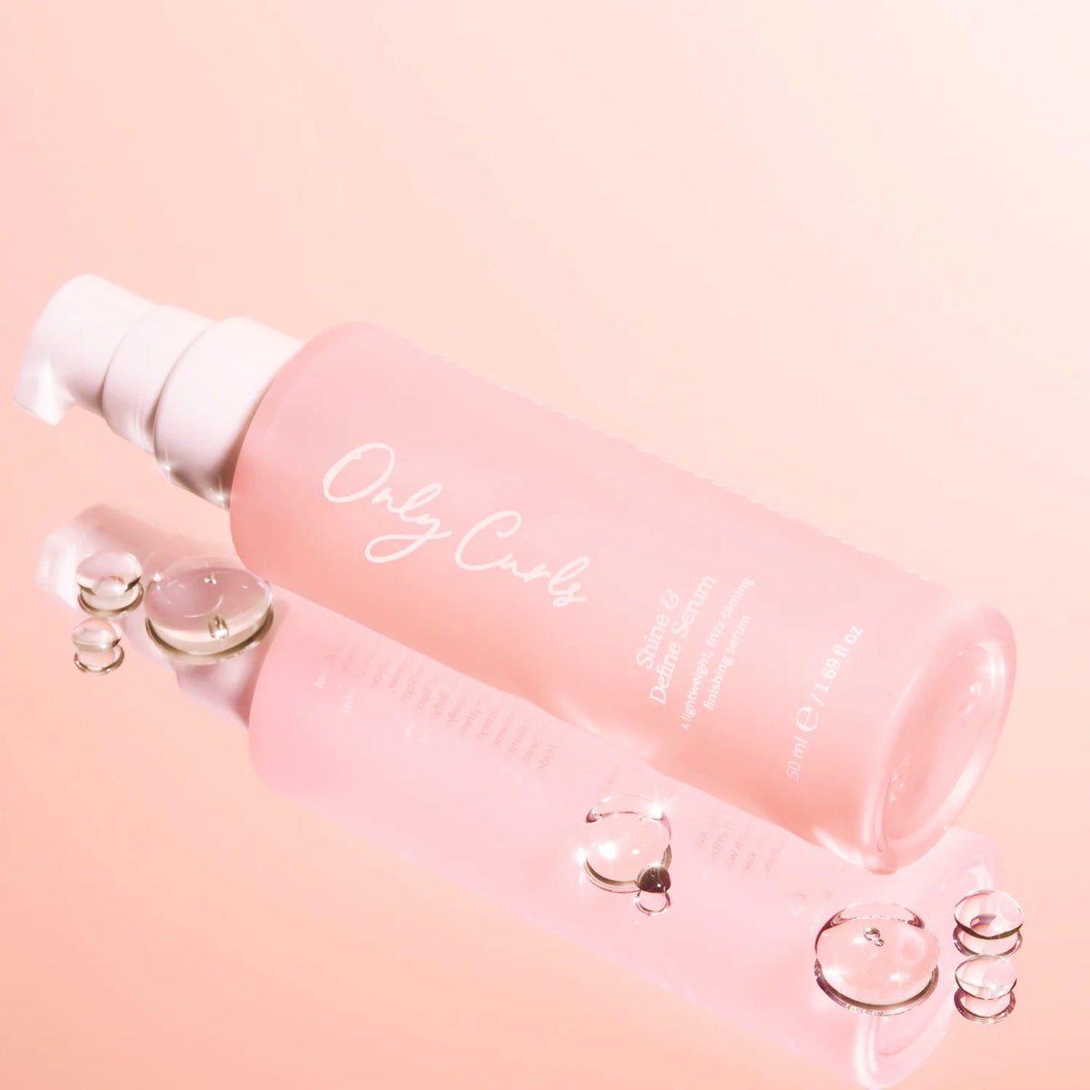 Only Curls Shine & Define Serum i lyserød flaske med pumpe, omgivet af klare serumdråber på lyserød baggrund.