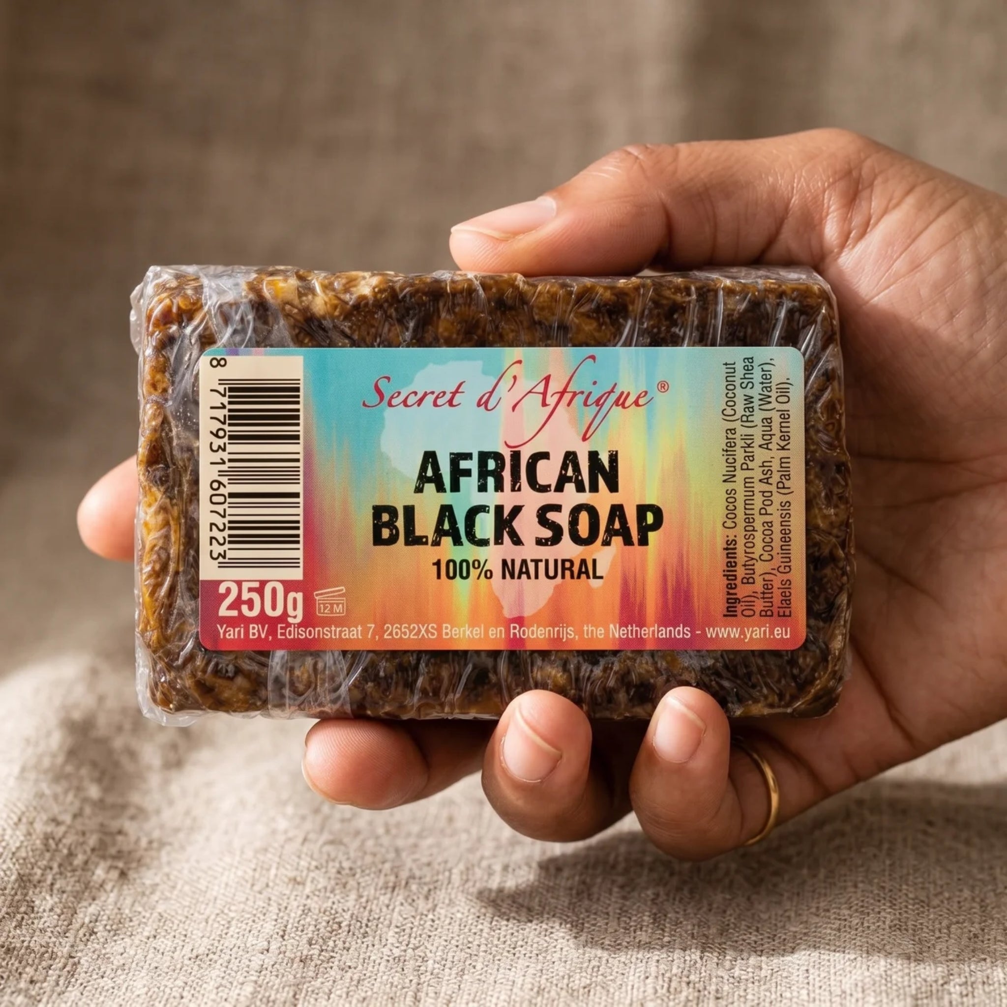 Hånd holder Secret d'Afrique African Black Soap, 250g sæbebar med naturligt mørkt udseende og etiket.