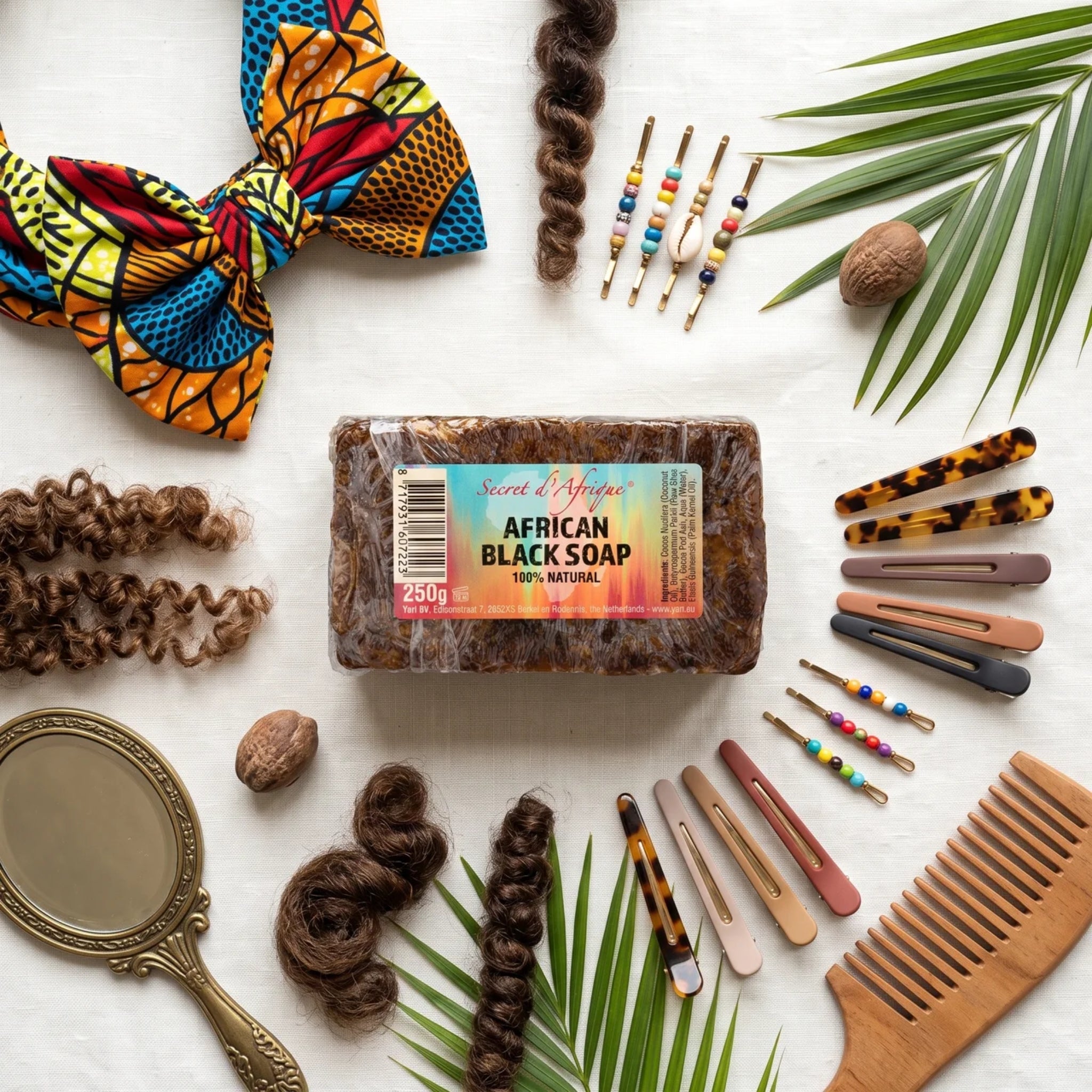 Secret d'Afrique African Black Soap 250g omgivet af hårspænder, afrikansk turban, krøllet hår og træ hårkam.