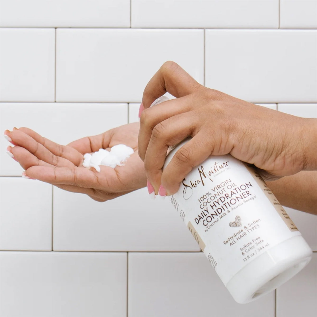 En hånd holder en portion af Shea Moisture 100% Virgin Coconut Oil Daily Hydration Conditioner, 384ml. Balsammen er hvid og cremet.