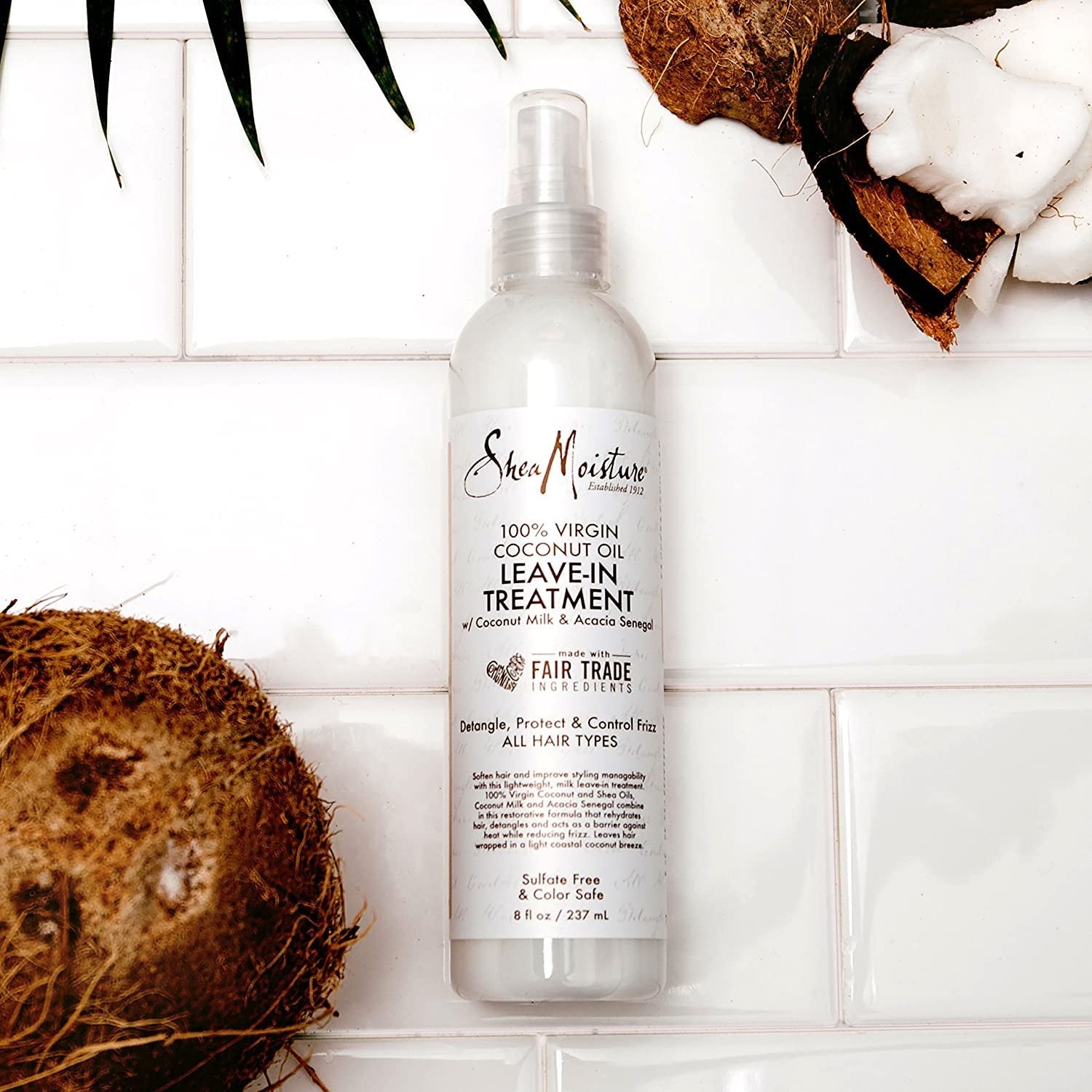 En sprayflaske med en hvid etikette. Produktet er Shea Moisture 100% Virgin Coconut Oil Daily Hydration Leave-In Treatment, 237ml. Leave-in conditioner til at detangle og reducere frizz i håret.