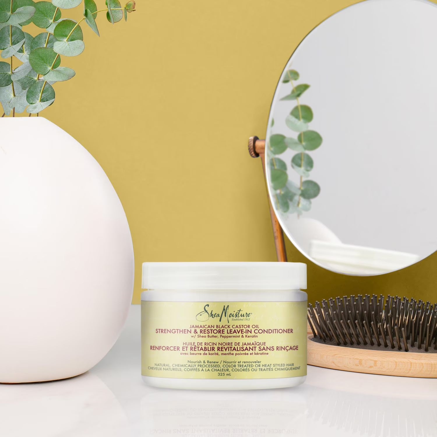 Nærbillede af Shea Moisture leave-in balsam i et lyst badeværelse med et rundt spejl og en træbørste.