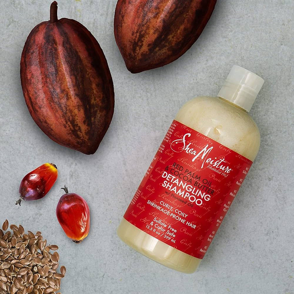 Shea Moisture Red Palm Oil & Cocoa Butter Hi-Slip Detangling Shampoo 399ml. Billedet viser shampooen sammen med rå ingredienser: kakaobønner, rød palmeolie og hørfrø.